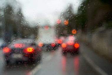Traffic stand still on a cold wet day, shot through a windshield, focusing on the raindrops, brake lights out of focus.