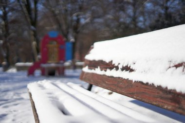 Beyaz kar bahçeli park bankı arka planda bulanık.