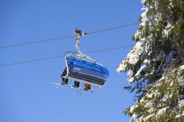 Feldberg, Almanya - 08 Şubat 2023: Leitner Ropeways mavi gökyüzüne karşı. Kış sporları meraklılarıyla dolu bir gondol. Karlı ve sarkıtlı fidan ağacı. Güneşli bir hava. Düşük açı. Kara Orman.