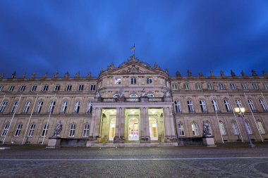 Stuttgart, Almanya - 26 Aralık 2023: Alacakaranlıkta açık mavi gökyüzü, aydınlık pencereler, kolonlar, heykeller ve merkezi bir kubbe ile büyük, klasik bir kale. Almanya, Stuttgart.