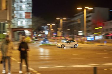 Stuttgart, Almanya - 26 Aralık 2023: Bulanık yayalar ve şehir ışıkları altında hareket eden bir arabayla Stuttgart 'ta dinamik bir gece sahnesi. Almanya, Stuttgart.