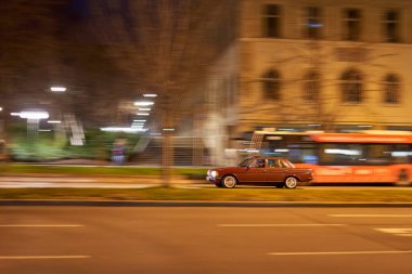 Stuttgart, Almanya - 26 Aralık 2023: Stuttgart 'ta hareket halindeki eski bir araba, gece vakti aydınlanmış bir otobüsün yanından geçiyor..