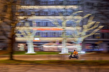 Geceleri Stuttgart 'ta motosikletli bir kişi. Arka planda bulanık hareket ve ışıklandırılmış ağaç şekilli ışıklar var. Noel, yeni doğan.