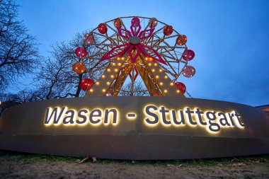 Stuttgart, Germany - December - 26, 2023: A brightly lit Ferris wheel at dusk with WASEN - STUTTGART illuminated in the foreground. Highlights Glanzlichter. Germany, Stuttgart. clipart