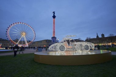 Stuttgart, Almanya - 26 Aralık 2023: Aydınlatılmış araba yapısı ve dönme dolabı, sütun üstüne heykel, halk etkinliği. Önemli noktalar (Glanzlichter). Almanya, Stuttgart.