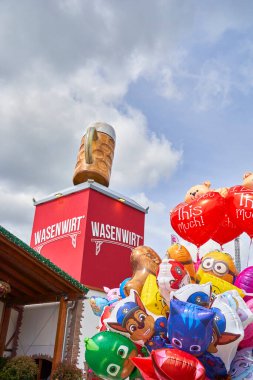 Stuttgart, Almanya - Mayıs - 06, 2023: Stuttgart bahar festivali: Parçalı bulutlu bir gökyüzü altında büyük bir dekoratif bira bardağı ve renkli balonlar içeren.