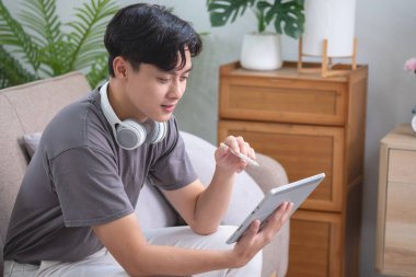 Rahatla, stres at, tatil yap, mutlu ol evde dinlenen, tabletten müzik dinleyen ve tablete yazmak için kalem tutan bir adam.