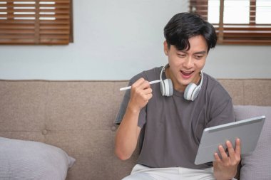 Rahatla, stres at, tatil yap, mutlu ol evde dinlenen, tabletten müzik dinleyen ve tablete yazmak için kalem tutan bir adam.