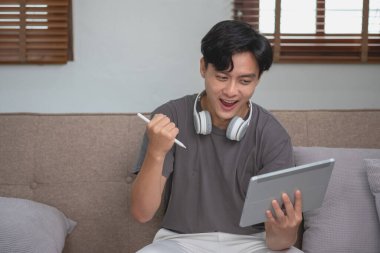 Rahatla, stres at, tatil yap, mutlu ol evde dinlenen, tabletten müzik dinleyen ve tablete yazmak için kalem tutan bir adam.