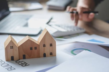 Muhasebeci, iş adamı, emlakçı, iş adamı müşterilere model ev veriyor. Müşterilerin imzalaması için ev faizi hesapları dökümanları da var..