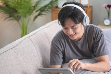 Elinde tabletle müzik dinleyen beyaz bir adamın portresi. Evde tatilde dinlenmek için evin içindeki kanepede bir kalem tutuyor..