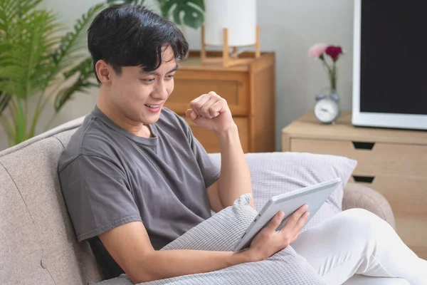 stock image Portrait of a white man listening to music with a tablet in hand holding a pen on the sofa inside the house to relax on vacation inside the house.