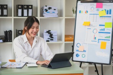 Portrait of a female accountant using a calculator and laptop to calculate balance using graphs for customers.