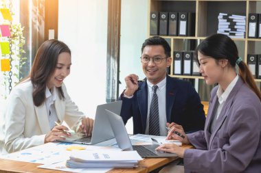 Bir grup işadamı, kazançları için dizüstü bilgisayarları ve grafik çizelgeleriyle plan yapar ve şirketlerini hesaplamak için bir hesap makinesi kullanır..