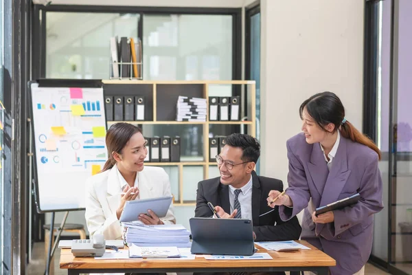 stock image Asian business team consists of marketing staff. accountant and financial officer Help each other analyze company profits using tablets. calculator Laptop computers, graph paper, and corporate pens.