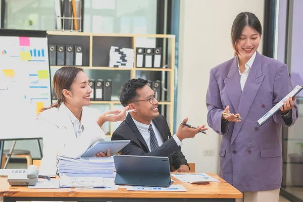 stock image Asian business team consists of marketing staff. accountant and financial officer Help each other analyze company profits using tablets. calculator Laptop computers, graph paper, and corporate pens.