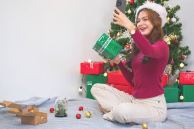 Mutlu Noeller ve mutlu tatiller! Kırmızı gömlekli güzel bir yüzü olan genç bir kadın Noel ağacı süslenmiş bir evde hediye kutularıyla neşe gösteriyor. Xmas 'tan Önce Portre