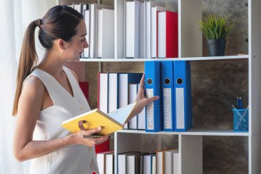 Asyalı iş kadını iş verilerini grafiklerle, sarı defterle el ele tutuşan grafiklerle ve ofisteki masada duran iş belgeleriyle sunuyor..