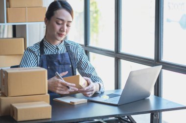 Asyalı bir iş kadını, internet üzerinden ürün satarak, çevrimiçi bir mağaza açarak ve ofis içinde müşteri paketlerinden sipariş alarak KOBİ işini seviyor. KOBİ İş Konsepti.