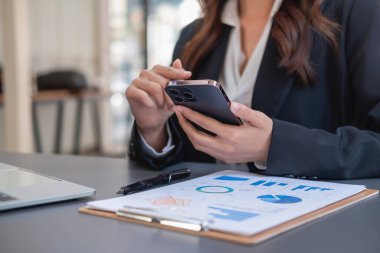 Siyahlı Asyalı iş kadını müşterilerle iletişim kurmak için cep telefonu kullanıyor. Hayat sigortası giderlerini ve amcasının laptopunu ofis sağlık sigortası konseptine kaydediyor.
