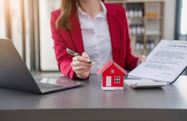 Muhasebeci, iş adamı, emlakçı, iş adamı müşterilere model ev veriyor. Müşterilerin imzalaması için ev faizi hesapları dökümanları da var..