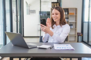 Pazarlama, Finans, Muhasebe, Planlama. Kafkasyalı iş kadını cep telefonu tutuyor ve şirkete katılan müşterilerin iyi niyetini gösteriyor. Laptop ofis ve belgelerinin kârını artırmak için.