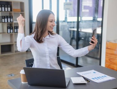 Pazarlama, Finans, Muhasebe, Planlama. Kafkasyalı iş kadını cep telefonu tutuyor ve şirkete katılan müşterilerin iyi niyetini gösteriyor. Laptop ofis ve belgelerinin kârını artırmak için.