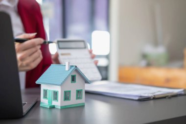 Muhasebeci, iş adamı, emlakçı, iş adamı müşterilere model ev veriyor. Müşterilerin imzalaması için ev faizi hesapları dökümanları da var..