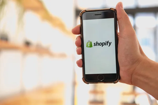 CHIANG MAI, THAILAND - 13 Ocak 2023: Bir kadın fırın ve kahve dükkanındaki ekranda Shopify uygulaması olan iPhone 8 ve cep telefonu bulunduruyor. Shopify çevrimiçi mağazalar için bir e-ticaret platformu.