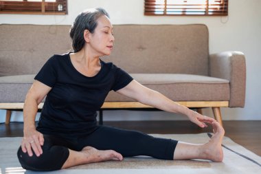 Asyalı yaşlı bir kadın iyi sağlık için yoga yaparken yaşlı bir kadın, rahatlatıcı bir günde evde vücudunun sağlığıyla ilgilenir. iyi sağlık kavramı