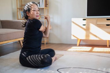 Asyalı yaşlı bir kadın iyi sağlık için yoga yaparken yaşlı bir kadın, rahatlatıcı bir günde evde vücudunun sağlığıyla ilgilenir. iyi sağlık kavramı