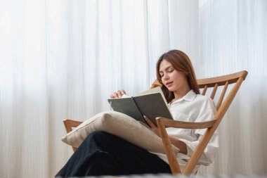 Güzel yüzlü, beyaz tişörtlü genç bir kadının portresi. Evindeki tahta sandalyeye oturmuş günlük tutuyor ve yazıyor. Dinlenme ve gevşeme kavramı..