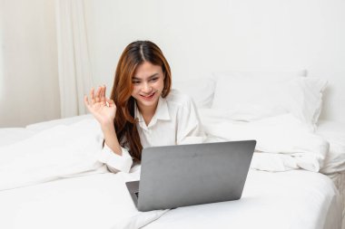 Beyaz gecelikli bir kadın hafta sonu uyanıp dinleniyor ve cep telefonuyla oynuyor ekmek yiyor ve beyaz yatak odasında çay içiyor. Sabah tatili.