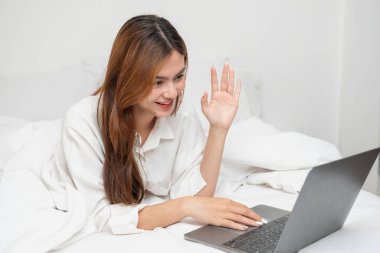 Beyaz gecelikli bir kadın hafta sonu uyanıp dinleniyor ve cep telefonuyla oynuyor ekmek yiyor ve beyaz yatak odasında çay içiyor. Sabah tatili.