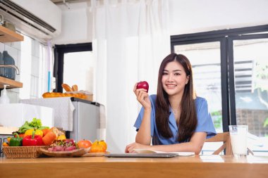 Mavi tişörtlü, güzel yüzlü, uzun saçlı, evde meyve yiyen bir genç kadın. Rahatlamak için dizüstü bilgisayar ve not defteriyle evde oturuyor.. 