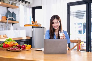 Mavi tişörtlü, güzel yüzlü, uzun saçlı, evde meyve yiyen bir genç kadın. Rahatlamak için dizüstü bilgisayar ve not defteriyle evde oturuyor.. 