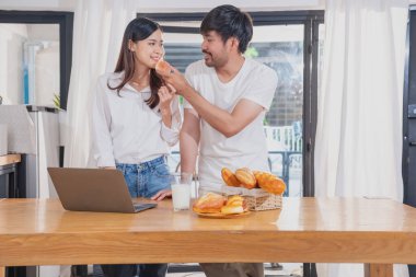 Meyve sebzelerle yemek yapan ve mutfakta dizüstü bilgisayar kullanan genç Asyalı çift aile içinde birlikte yemek pişiriyor. Aile kavramı..