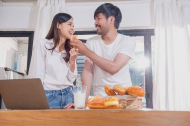 Meyve sebzelerle yemek yapan ve mutfakta dizüstü bilgisayar kullanan genç Asyalı çift aile içinde birlikte yemek pişiriyor. Aile kavramı..