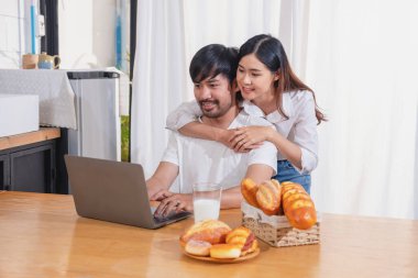 Meyve sebzelerle yemek yapan ve mutfakta dizüstü bilgisayar kullanan genç Asyalı çift aile içinde birlikte yemek pişiriyor. Aile kavramı..