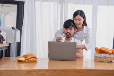 Meyve sebzelerle yemek yapan ve mutfakta dizüstü bilgisayar kullanan genç Asyalı çift aile içinde birlikte yemek pişiriyor. Aile kavramı..