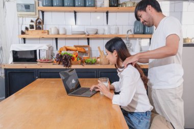 Meyve sebzelerle yemek yapan ve mutfakta dizüstü bilgisayar kullanan genç Asyalı çift aile içinde birlikte yemek pişiriyor. Aile kavramı..