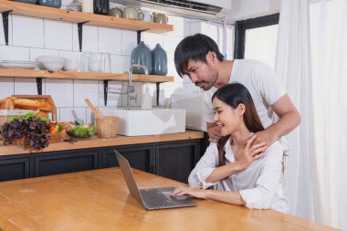 Meyve sebzelerle yemek yapan ve mutfakta dizüstü bilgisayar kullanan genç Asyalı çift aile içinde birlikte yemek pişiriyor. Aile kavramı..