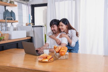Meyve sebzelerle yemek yapan ve mutfakta dizüstü bilgisayar kullanan genç Asyalı çift aile içinde birlikte yemek pişiriyor. Aile kavramı..