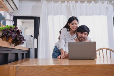 Meyve sebzelerle yemek yapan ve mutfakta dizüstü bilgisayar kullanan genç Asyalı çift aile içinde birlikte yemek pişiriyor. Aile kavramı..