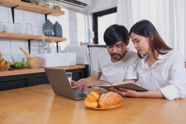 Meyve sebzelerle yemek yapan ve mutfakta dizüstü bilgisayar kullanan genç Asyalı çift aile içinde birlikte yemek pişiriyor. Aile kavramı..