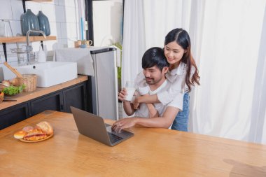 Meyve sebzelerle yemek yapan ve mutfakta dizüstü bilgisayar kullanan genç Asyalı çift aile içinde birlikte yemek pişiriyor. Aile kavramı..