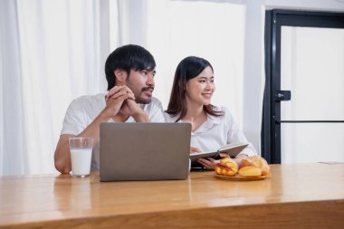 Meyve sebzelerle yemek yapan ve mutfakta dizüstü bilgisayar kullanan genç Asyalı çift aile içinde birlikte yemek pişiriyor. Aile kavramı..