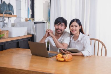 Meyve sebzelerle yemek yapan ve mutfakta dizüstü bilgisayar kullanan genç Asyalı çift aile içinde birlikte yemek pişiriyor. Aile kavramı..