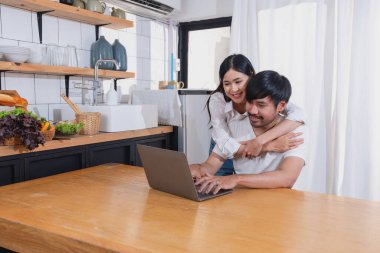 Meyve sebzelerle yemek yapan ve mutfakta dizüstü bilgisayar kullanan genç Asyalı çift aile içinde birlikte yemek pişiriyor. Aile kavramı..