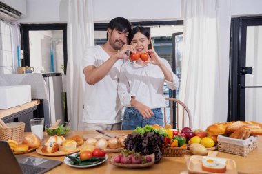 Meyve sebzelerle yemek yapan ve mutfakta dizüstü bilgisayar kullanan genç Asyalı çift aile içinde birlikte yemek pişiriyor. Aile kavramı..